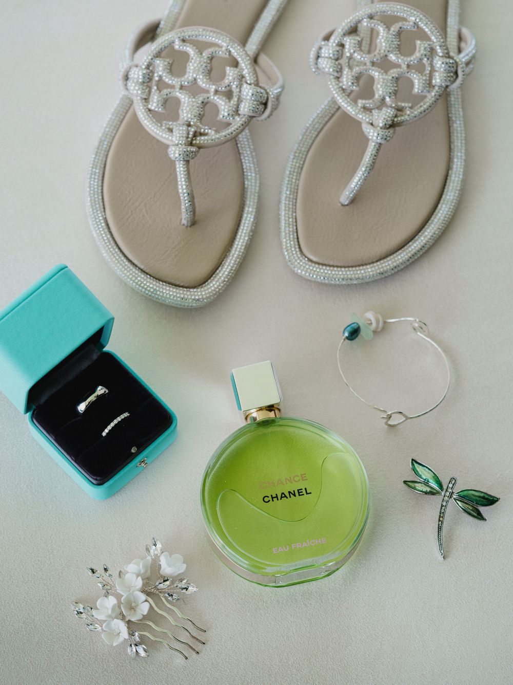 Wedding accessories including silver sandals, turquoise ring box, perfume, and jewelry laid out on white surface.