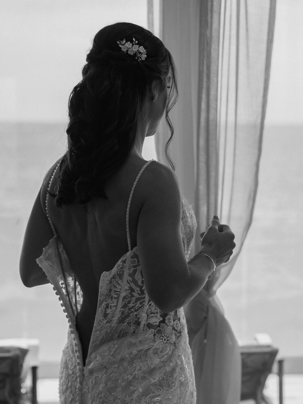 Back view of bride in lace dress looking out window.