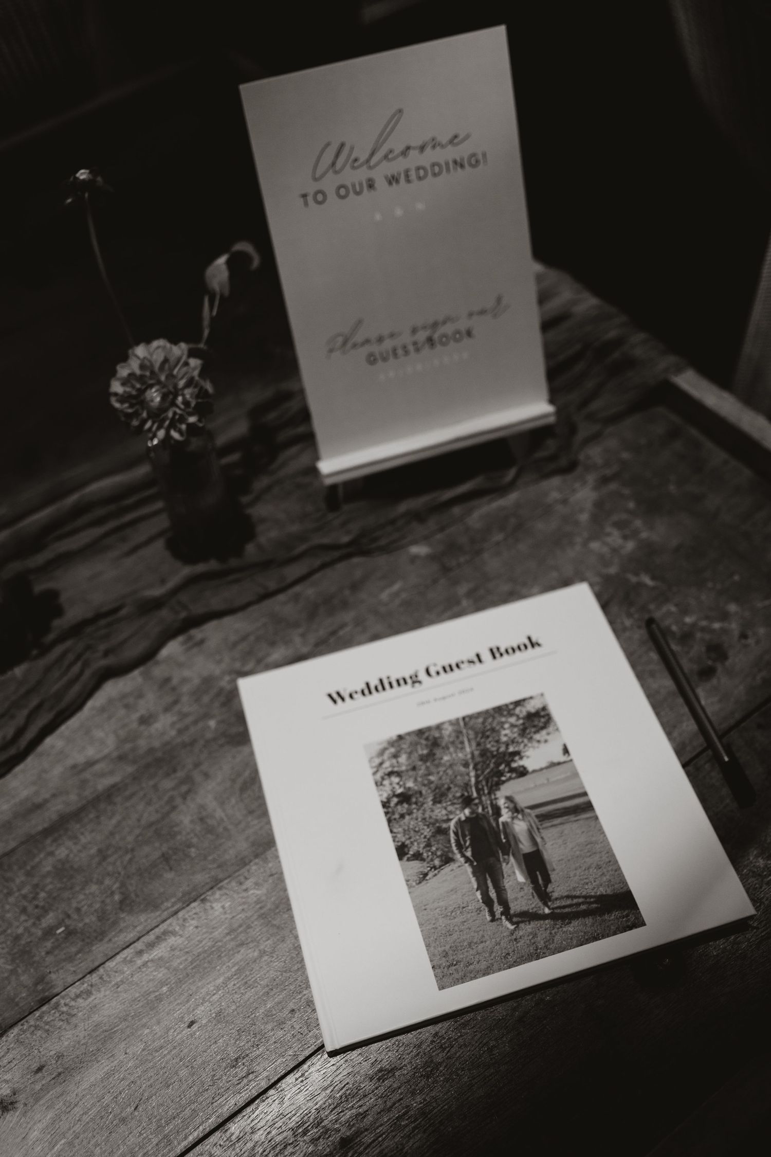 Black and white photo of wedding guest book and photo memories displayed on weathered wood in moody lighting.