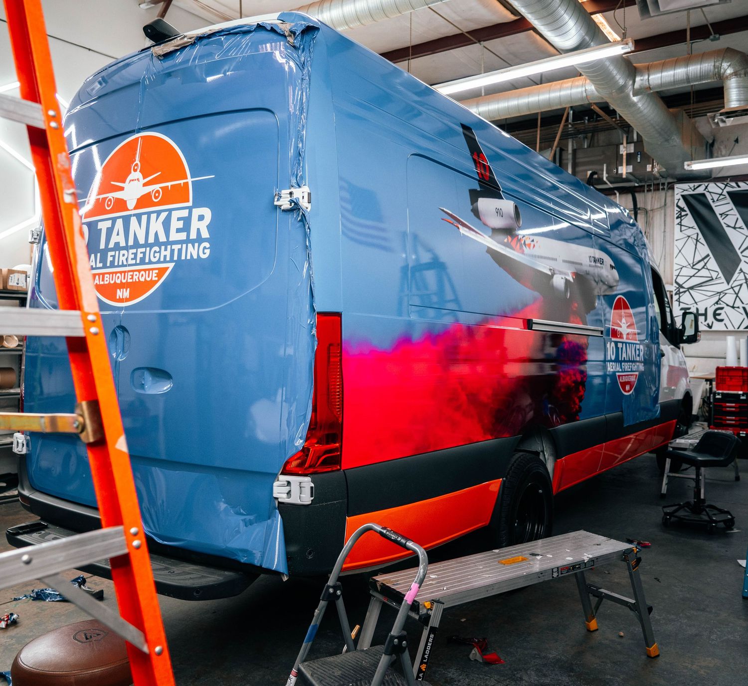 Large blue and red commercial delivery van being professionally wrapped with vinyl graphics for Tanker Maid Services.