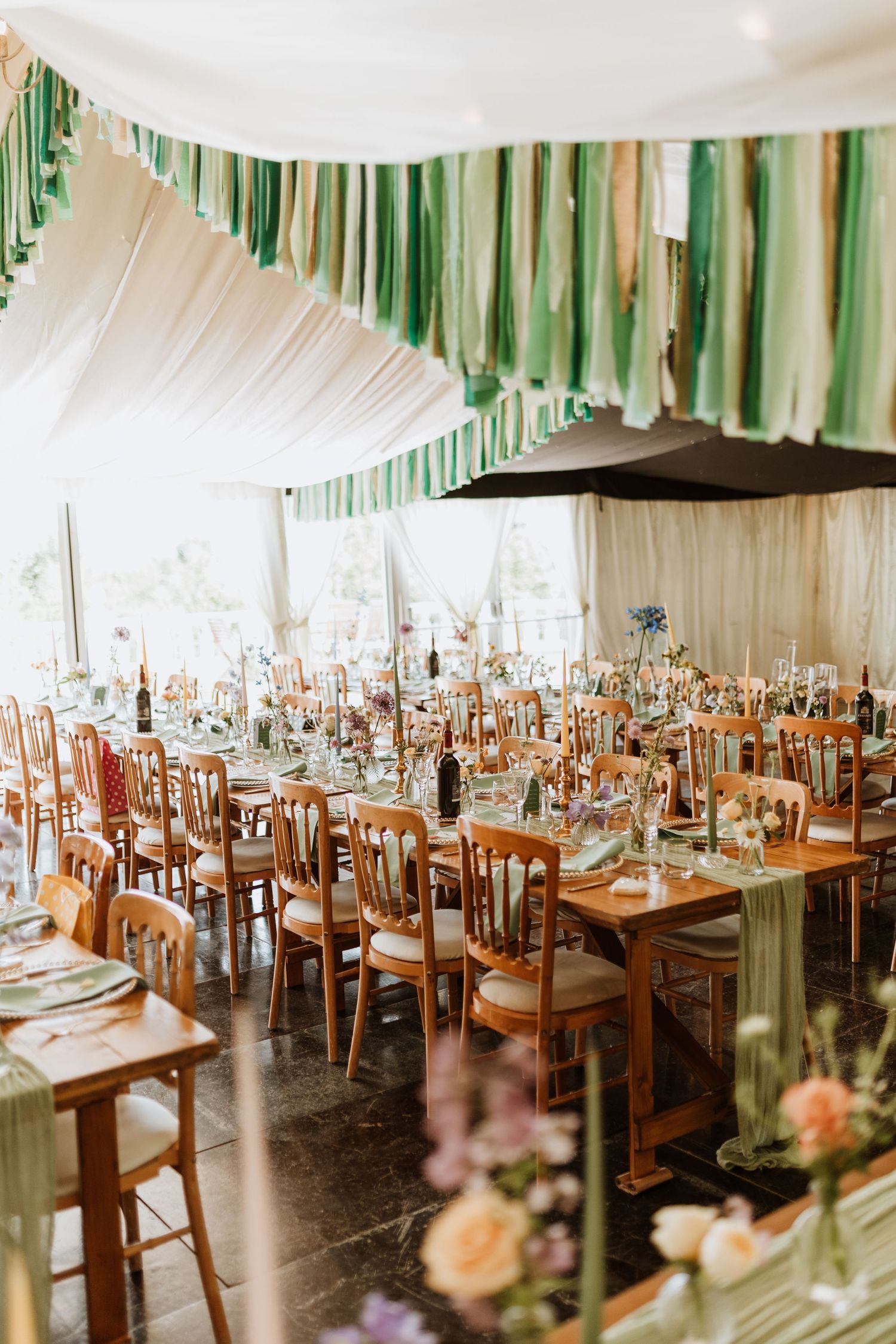 Wedding reception venue decorated with green ribbon streamers and white draping above wooden tables and chairs.