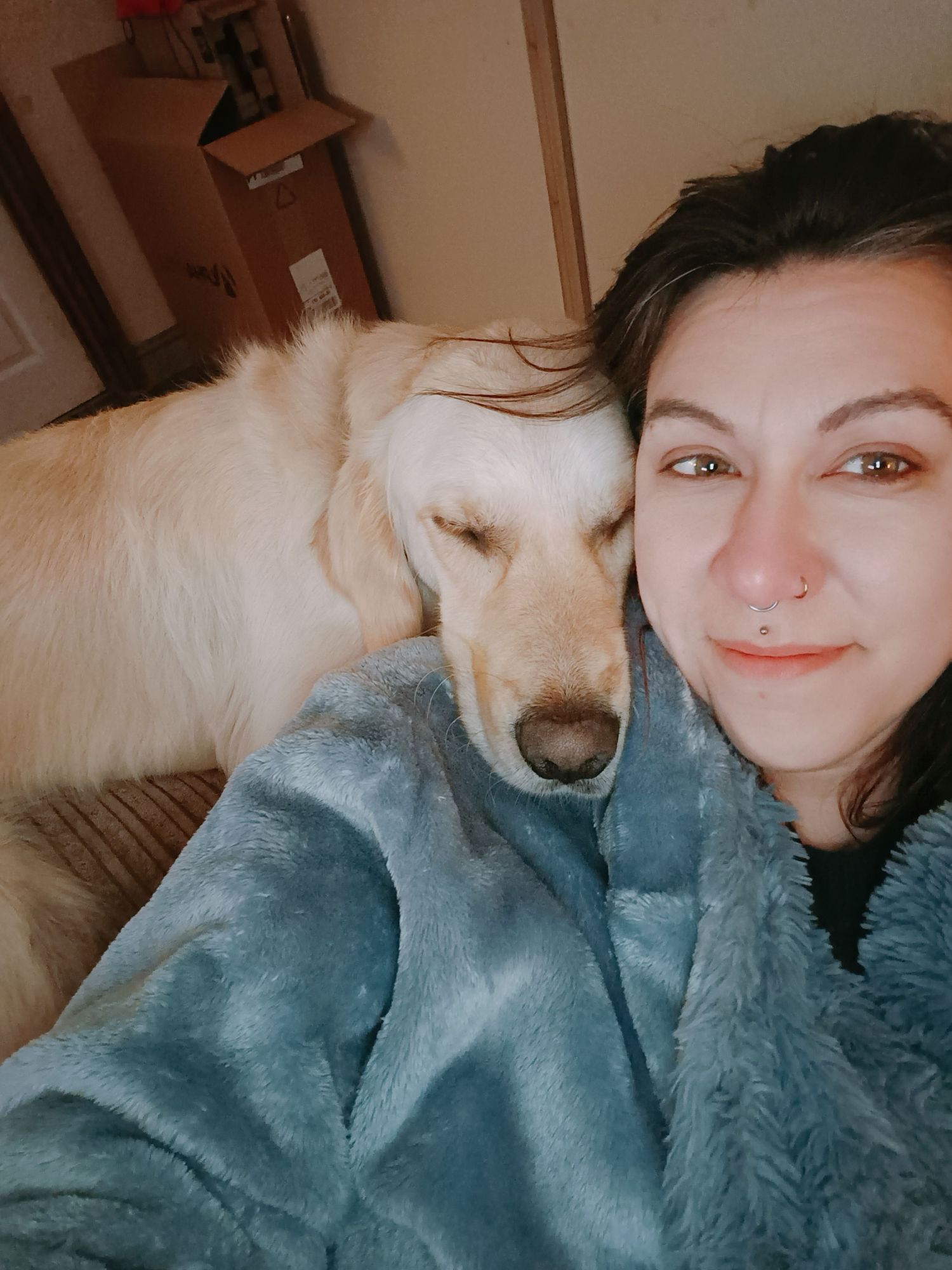 Person taking selfies with a white fluffy dog while relaxing on comfortable bedding.