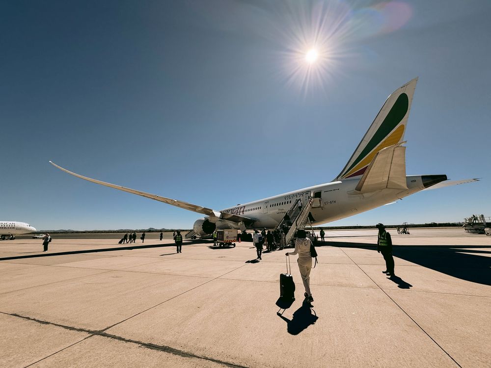 Passengers boarding Ethiopian Airlines plane on sunny tarmac with bright sun overhead.