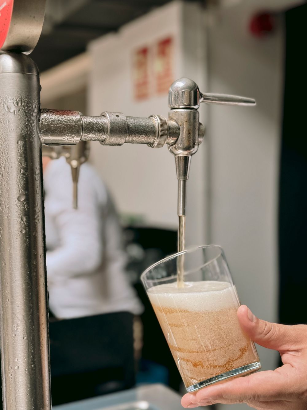 Bartender pouring fresh draft beer from tap into glass at a bar.