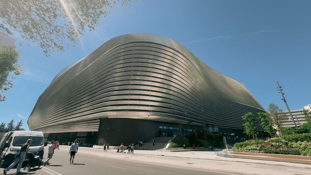 Futuristic curved metallic building with layered wave-like facade under blue sky.