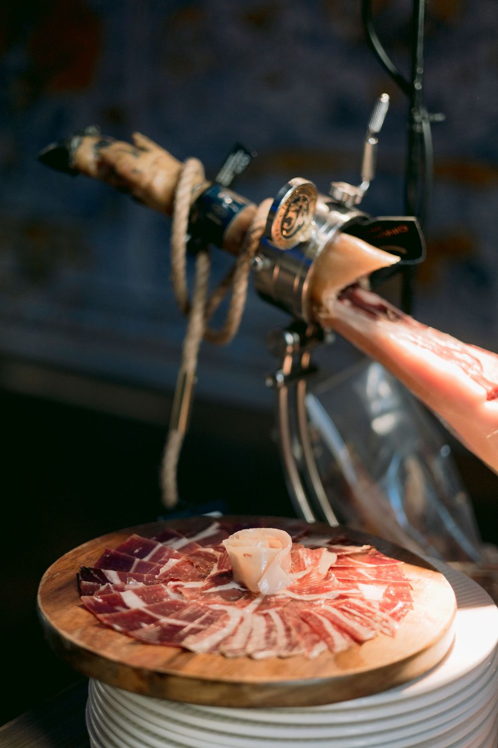 Thinly sliced Iberian jamon serrano on wooden board with meat carving holder.