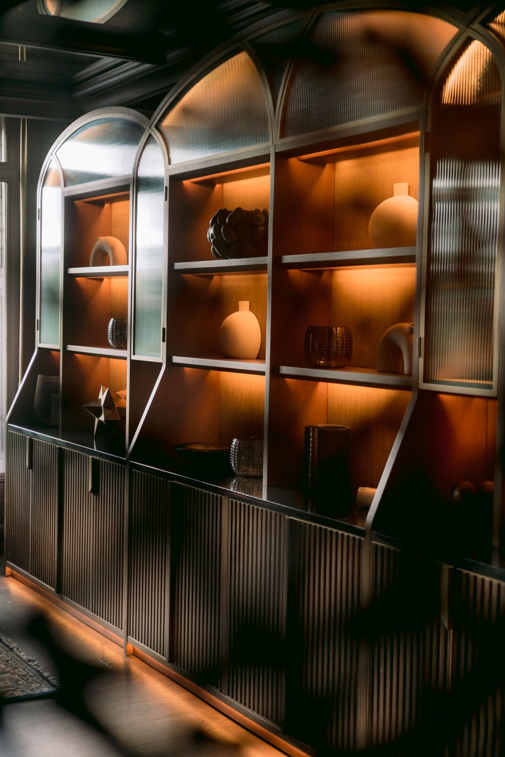 Illuminated arched display cabinet with warm amber lighting showcasing decorative vases.