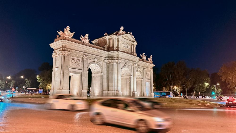 Puerta de Alcala monument illuminated at night with light trails from passing cars.