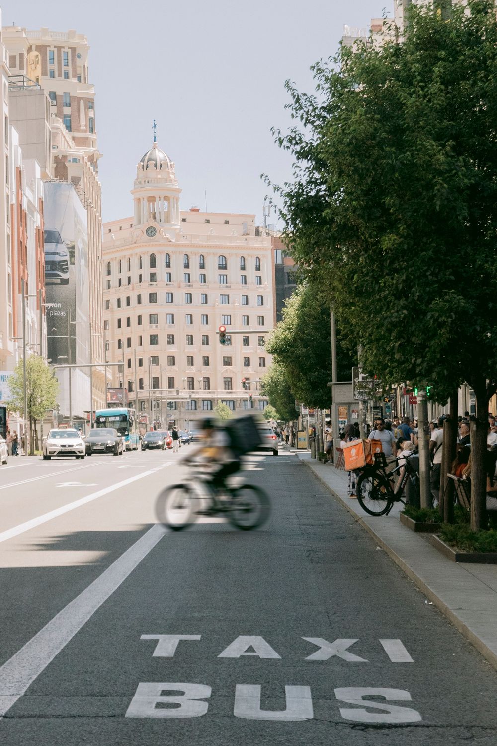Busy city street with taxi bus lane, cyclist, and historic building in background.