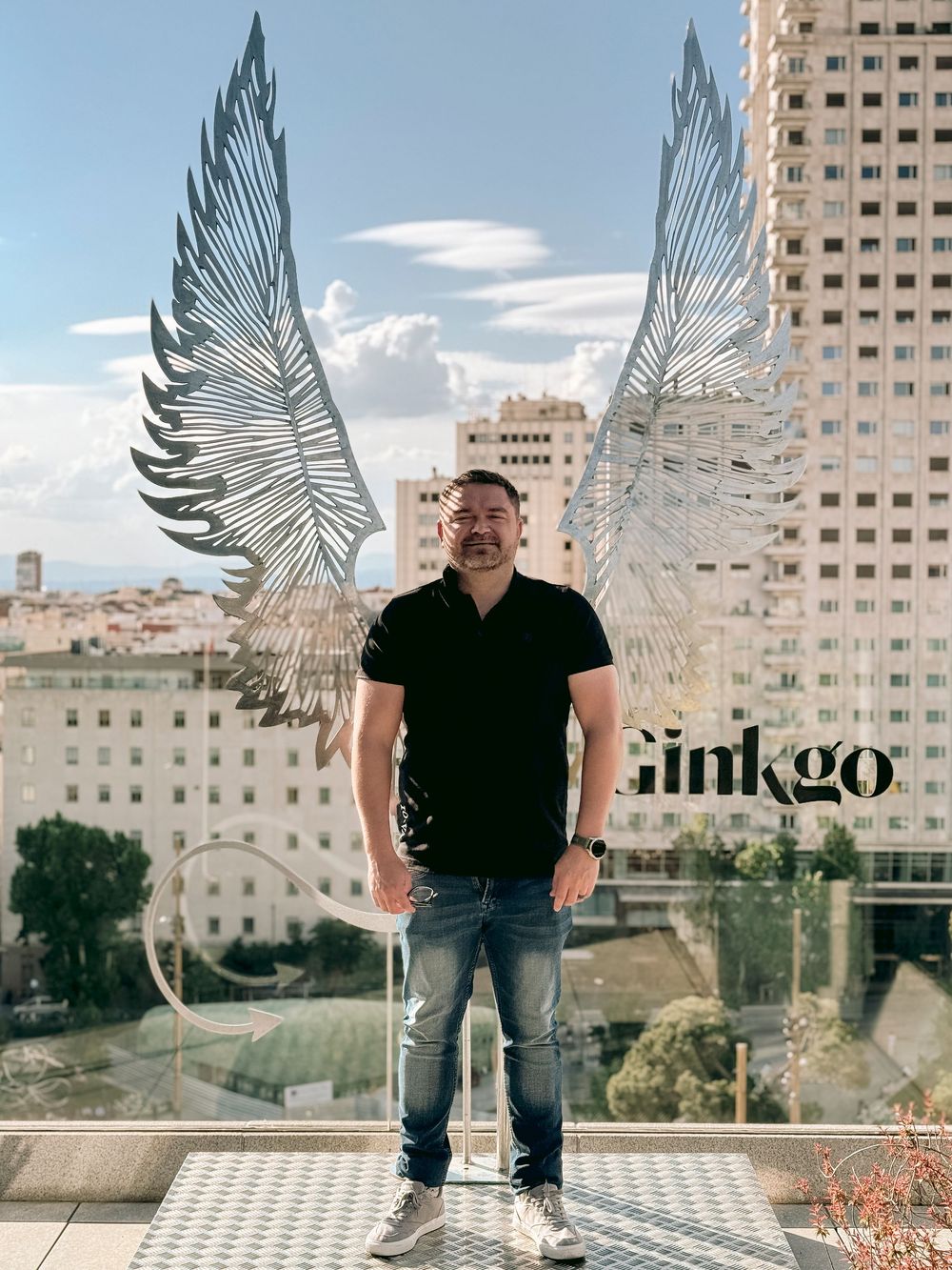 Man standing before large decorative metal angel wings at Ginkgo rooftop bar Madrid.