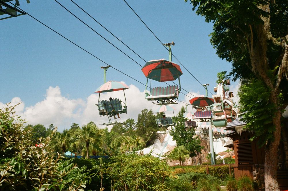 Colorful ski lift gondolas transport visitors over lush tropical vegetation against a bright blue sky.