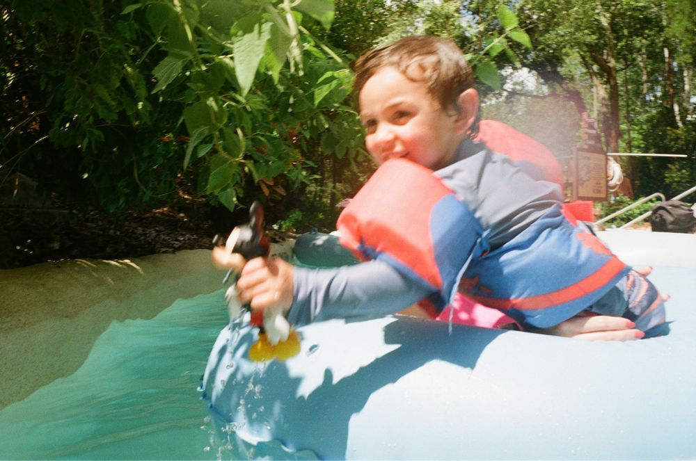 Someone wearing a blue life jacket splashes into the water while tubing on a summer day.