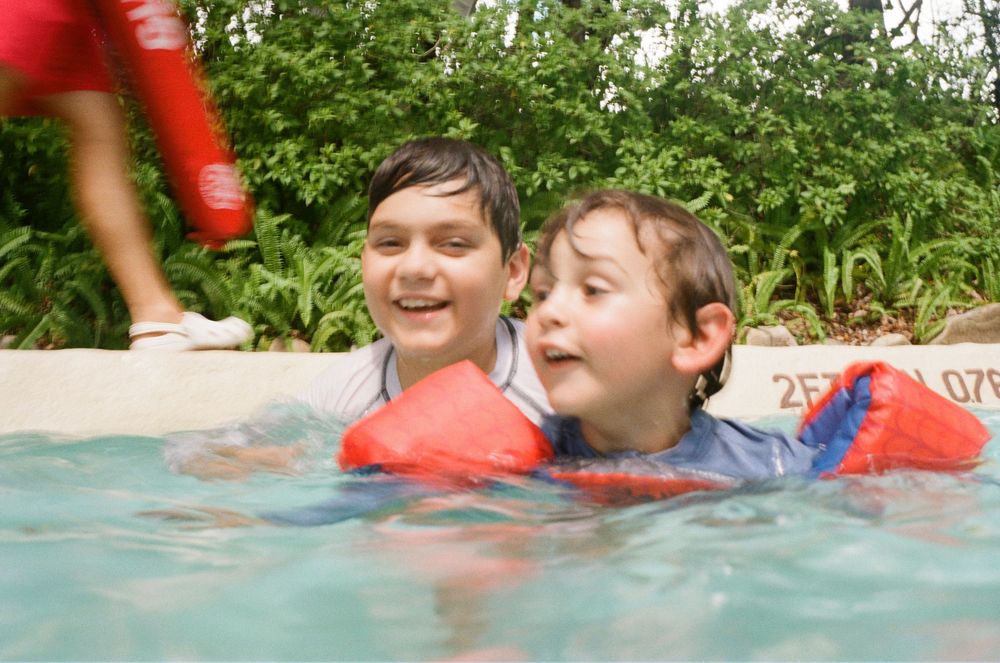 Several children swim and splash together in refreshing blue pool water on a sunny summer day.