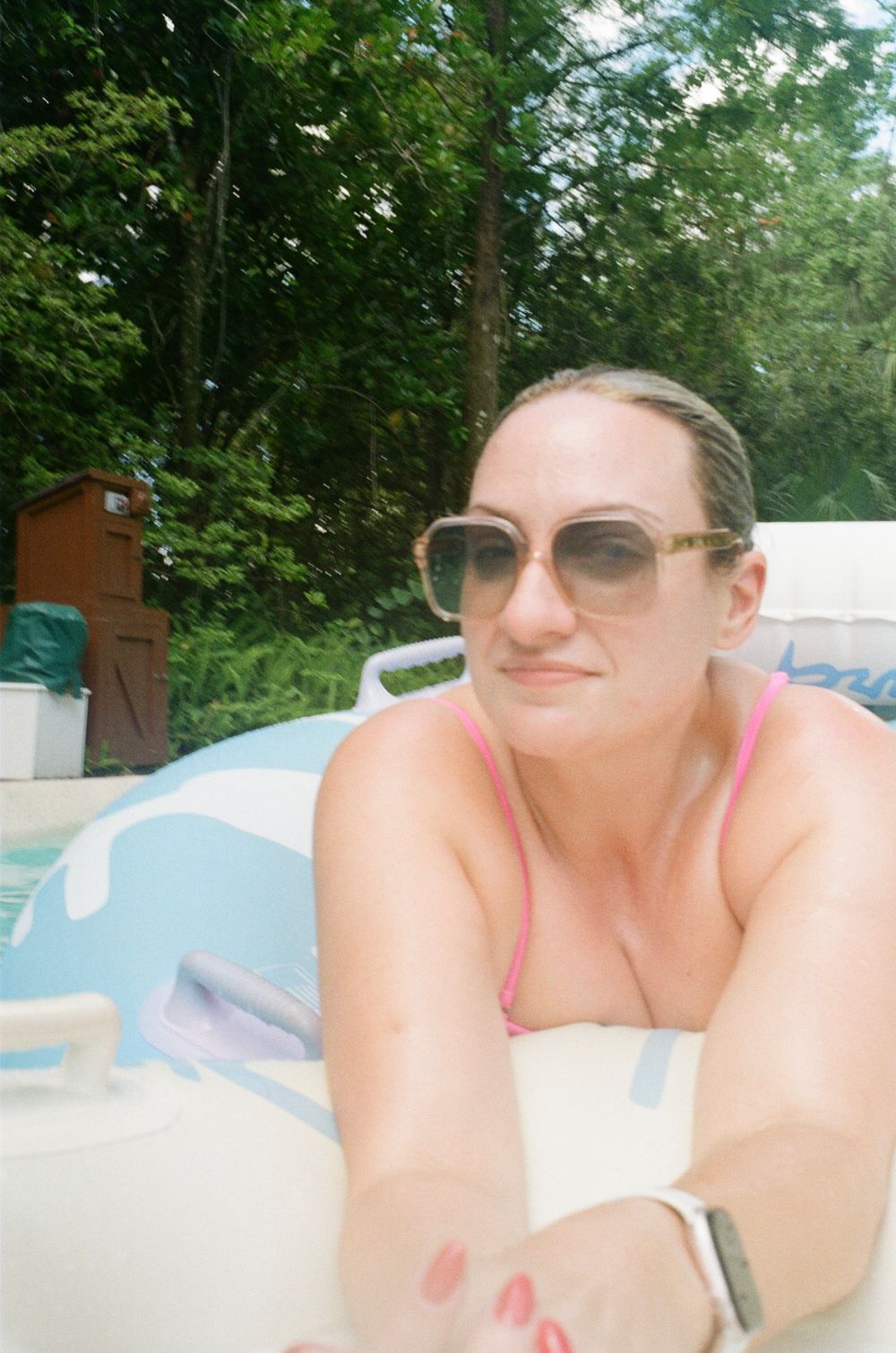 Someone wearing sunglasses and a pink top relaxes on a pool float on a sunny summer day.