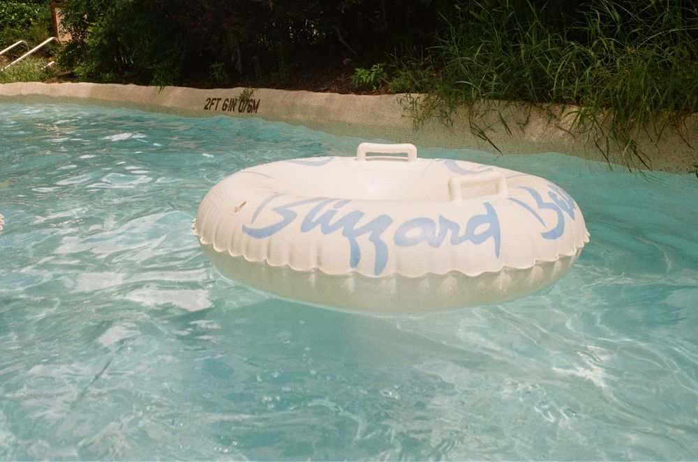 A large blue and white inflatable pool float drifts on the surface of turquoise swimming pool water.