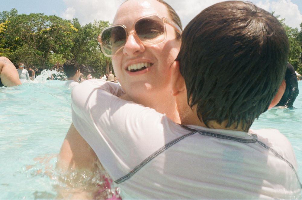 Three friends share a friendly embrace while enjoying a sunny day at a tropical beach with clear turquoise waters.