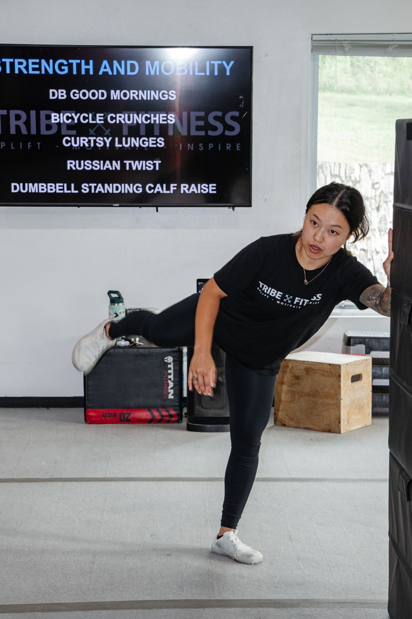 Instructor demonstrating a curtsy lunge with leg lifted exercise list displayed on screen behind her.