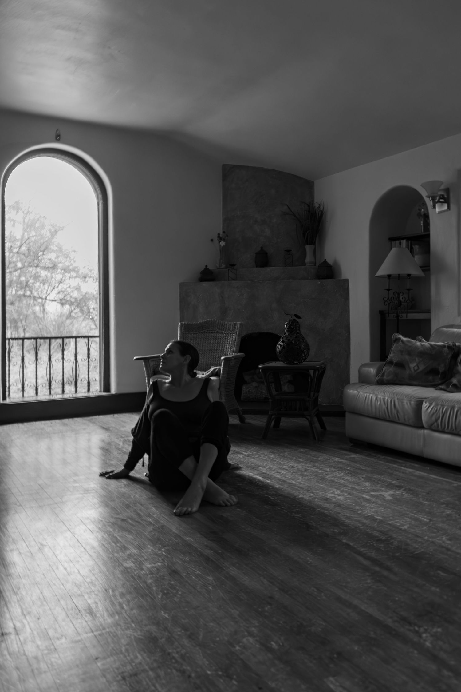 Empty dance studio interior with wooden floors and arched windows casting dramatic shadows.