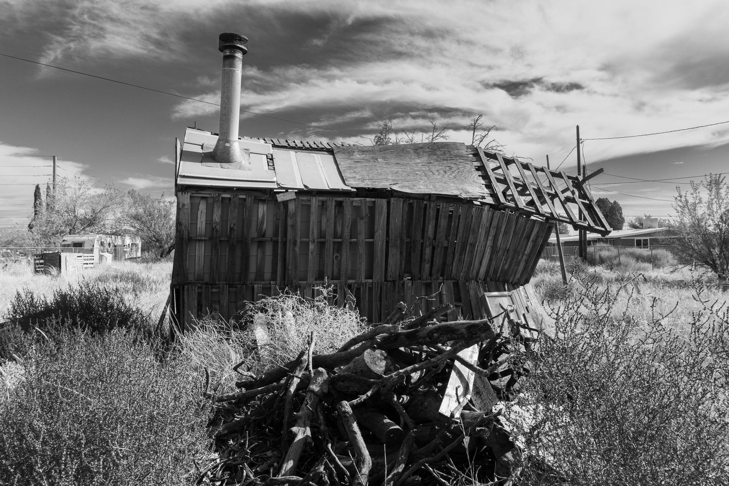 Rural landscape with abandoned structures and farm equipment under dramatic sky.