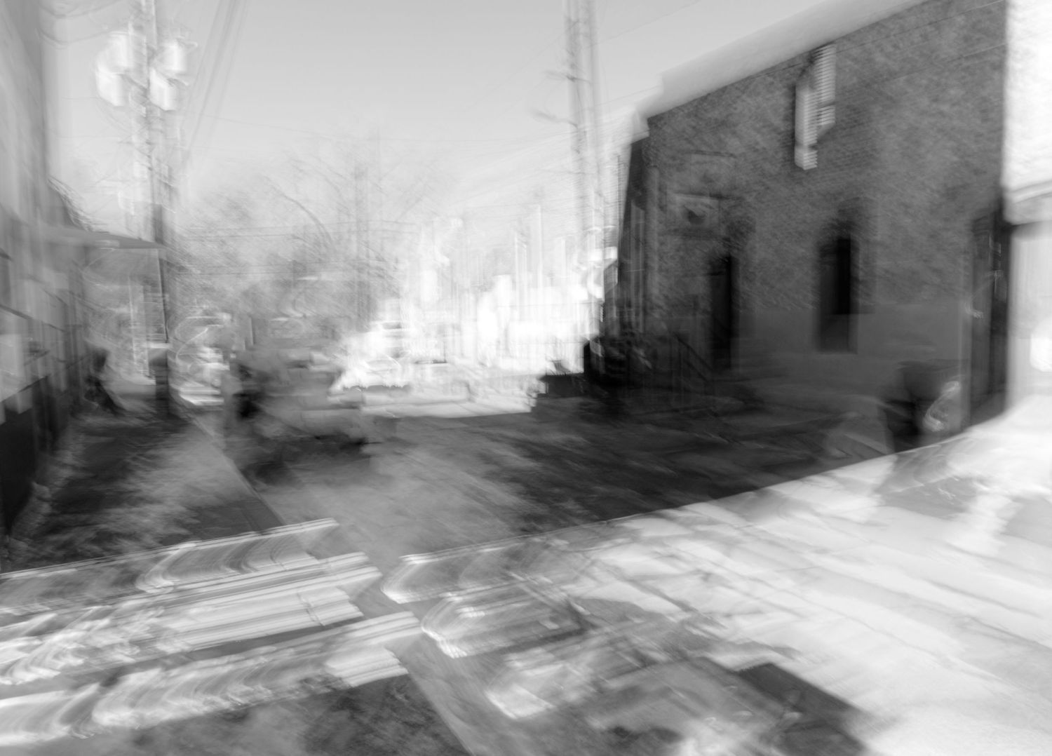 Blurry black and white urban street scene showing buildings and sidewalks in motion.