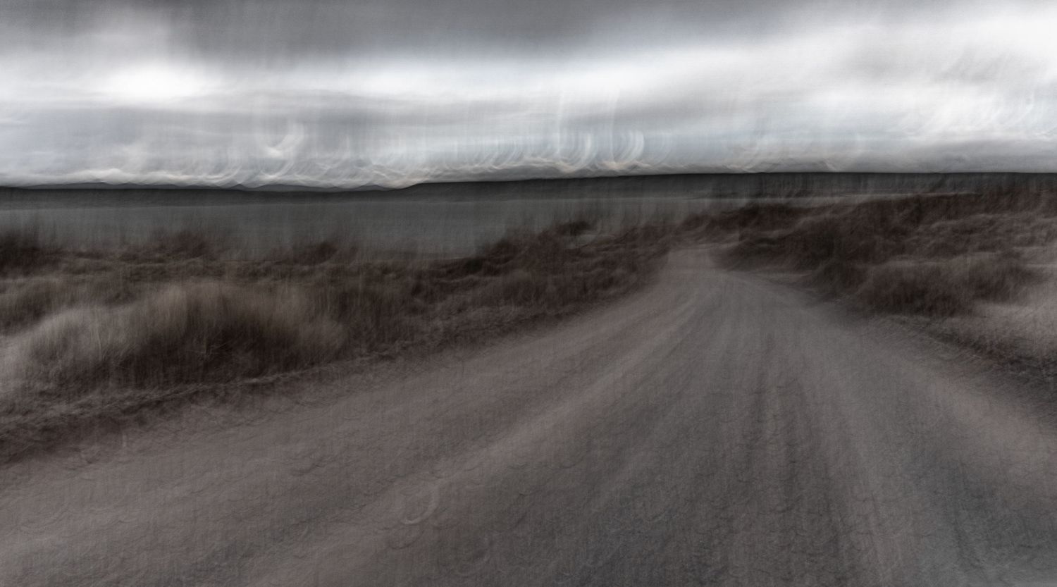 Atmospheric dirt road winding through misty rural landscape under cloudy skies.
