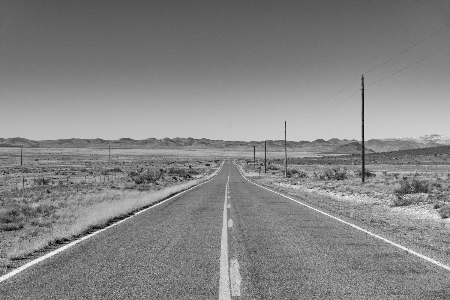 Empty desert highway stretching to horizon through barren landscape.