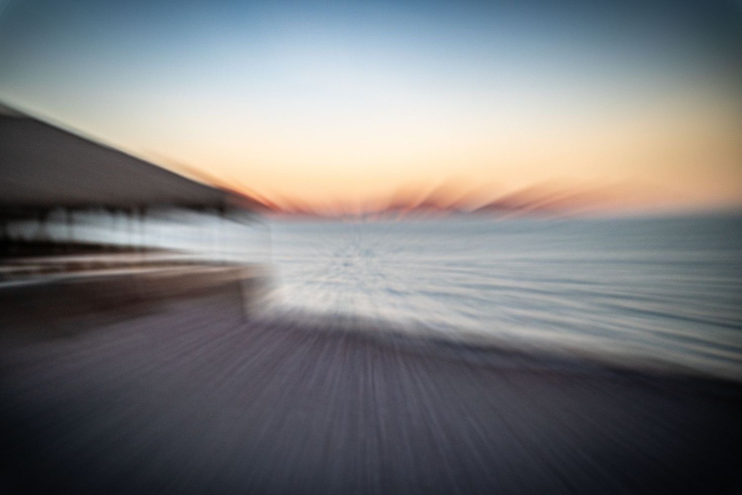 Blurred oceanfront boardwalk at sunset with dramatic sky.