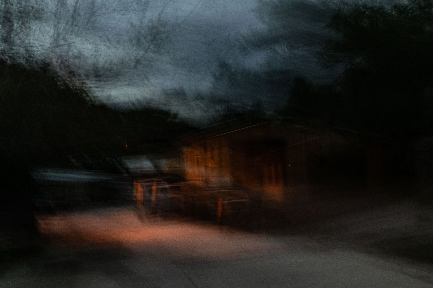 Blurred nighttime forest scene with warm orange lights glowing through dark trees.
