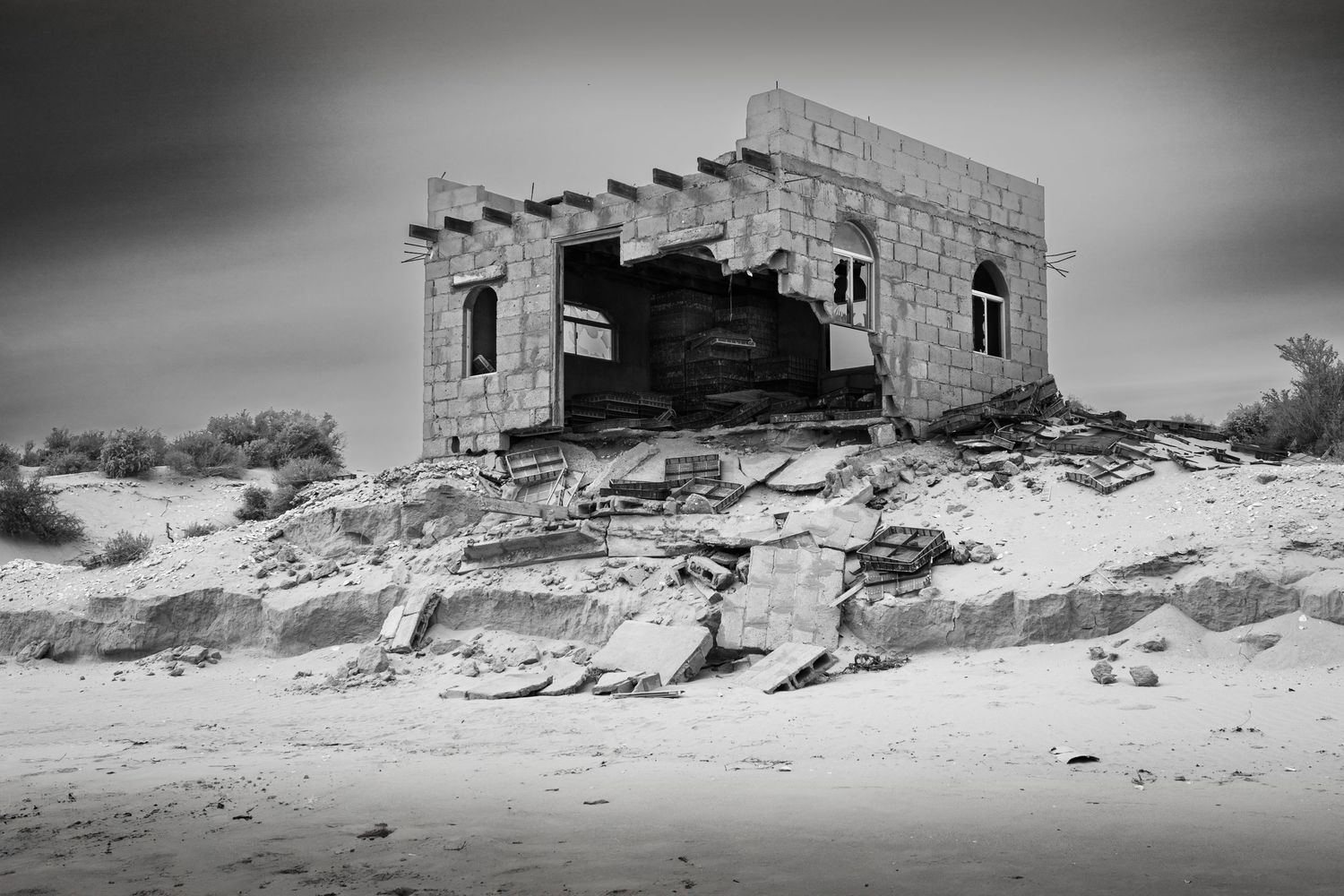 Abandoned concrete building deteriorating on sandy desert hill.