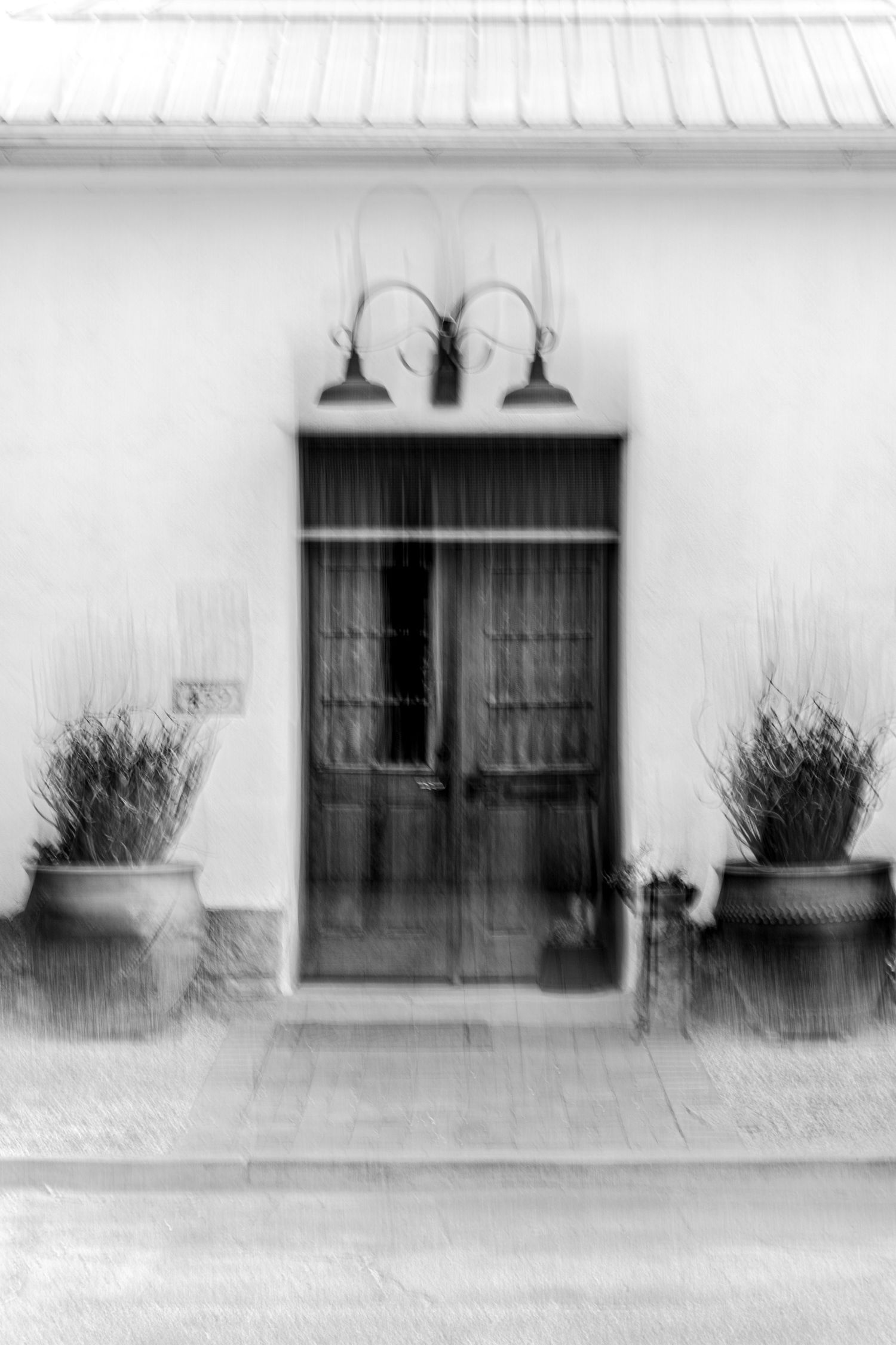 Minimalist black and white photograph of storefront windows and doors with wall sconces.