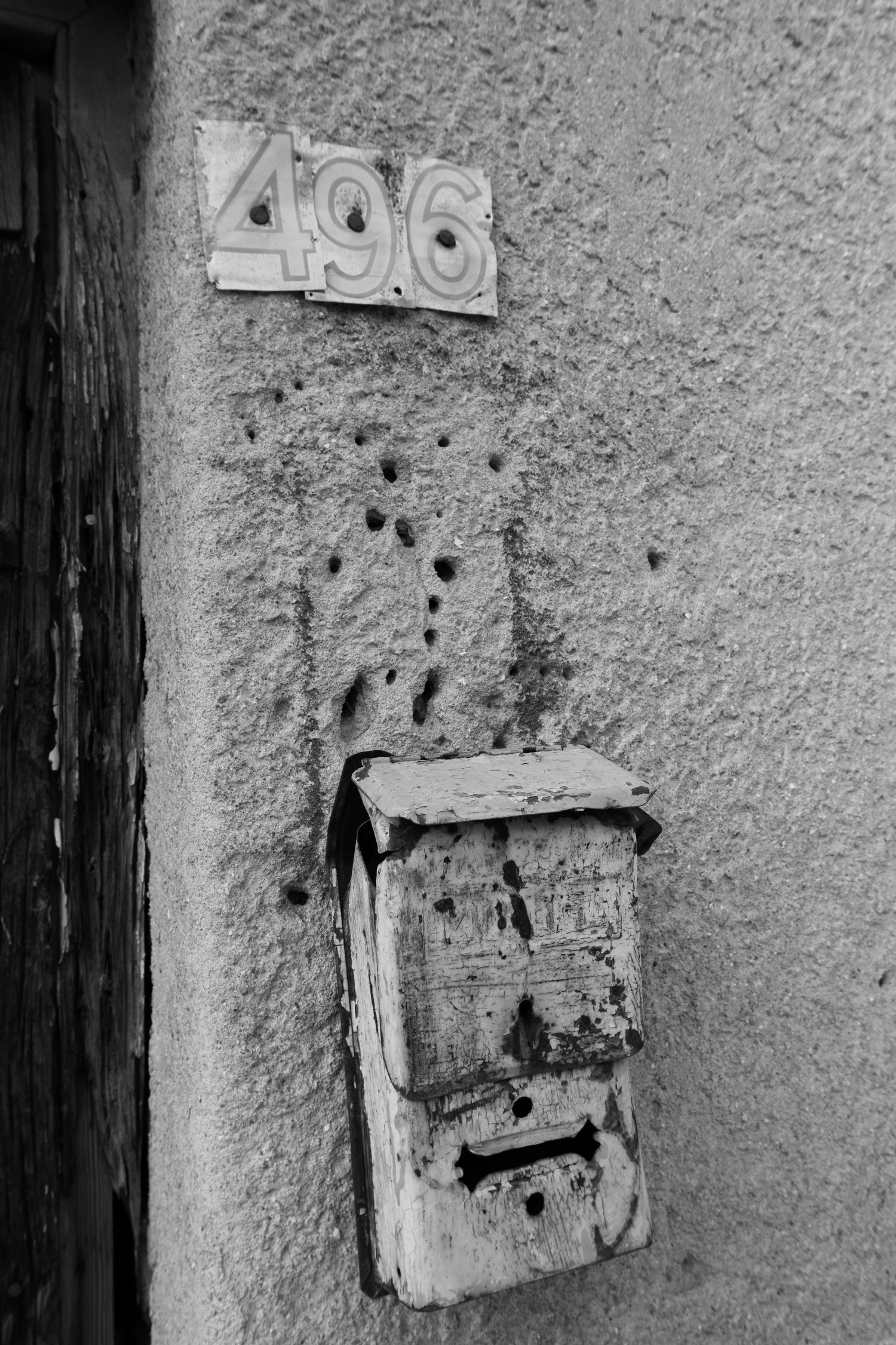 Weathered mailbox and house number 496 on textured wall with bullet holes.