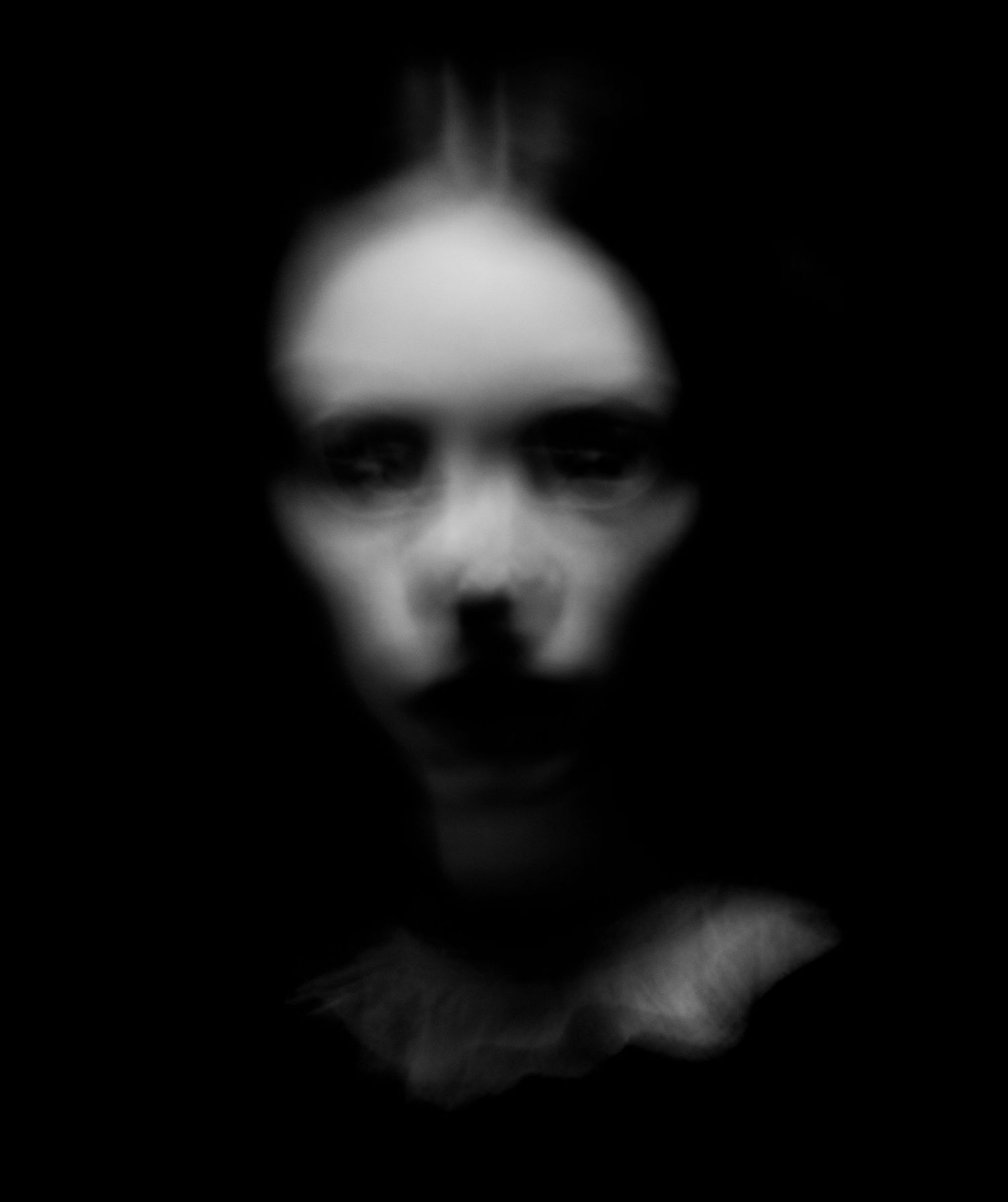 Blurry black and white portrait creating an ethereal, haunting mood in dark shadows.