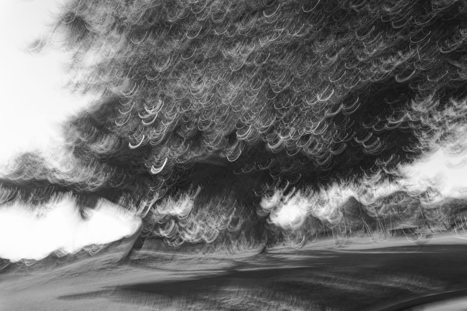 Abstract black and white cloudscape with dramatic swirling patterns against a light sky.