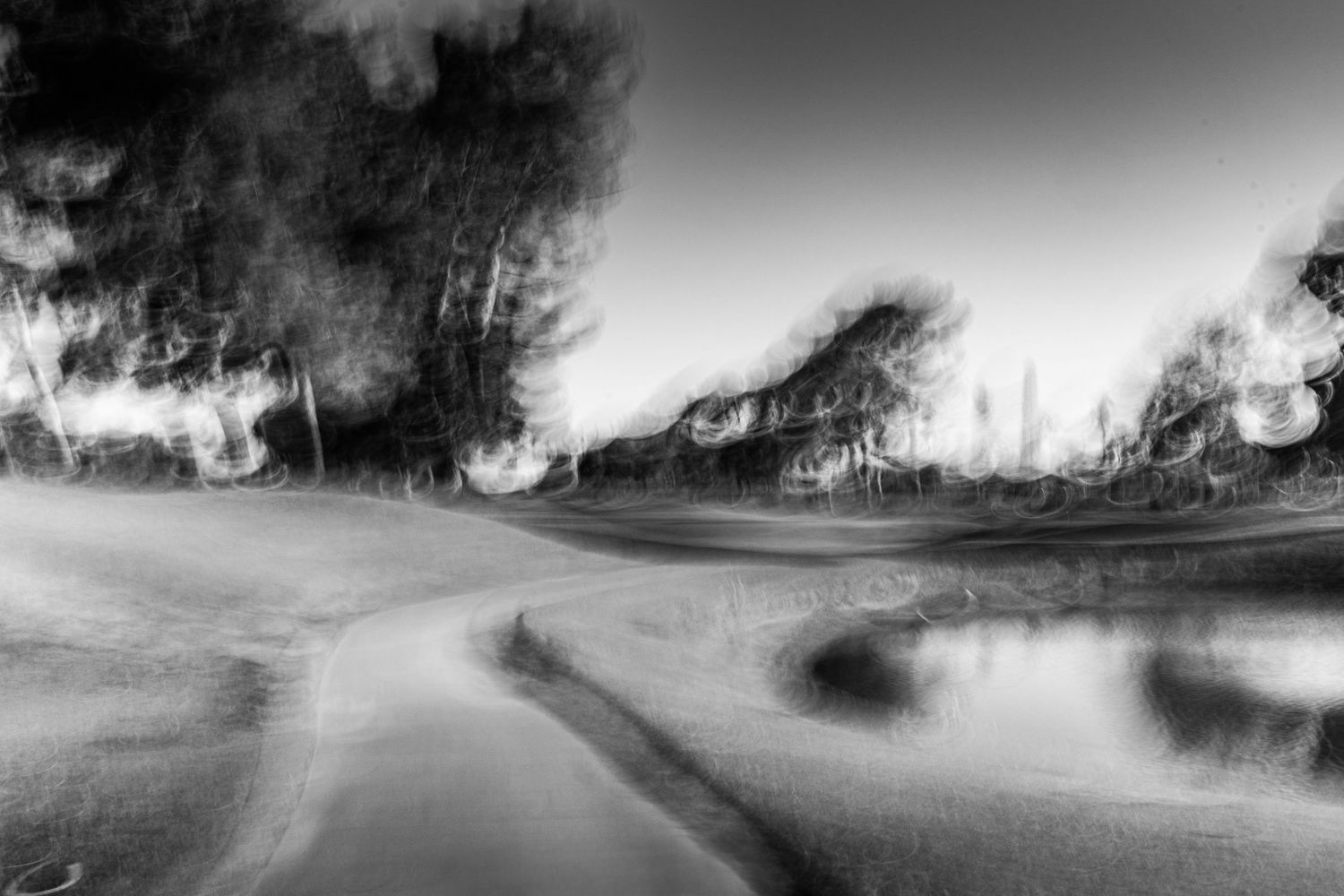 Artistic black and white motion blur photograph of a winding rural road through trees.