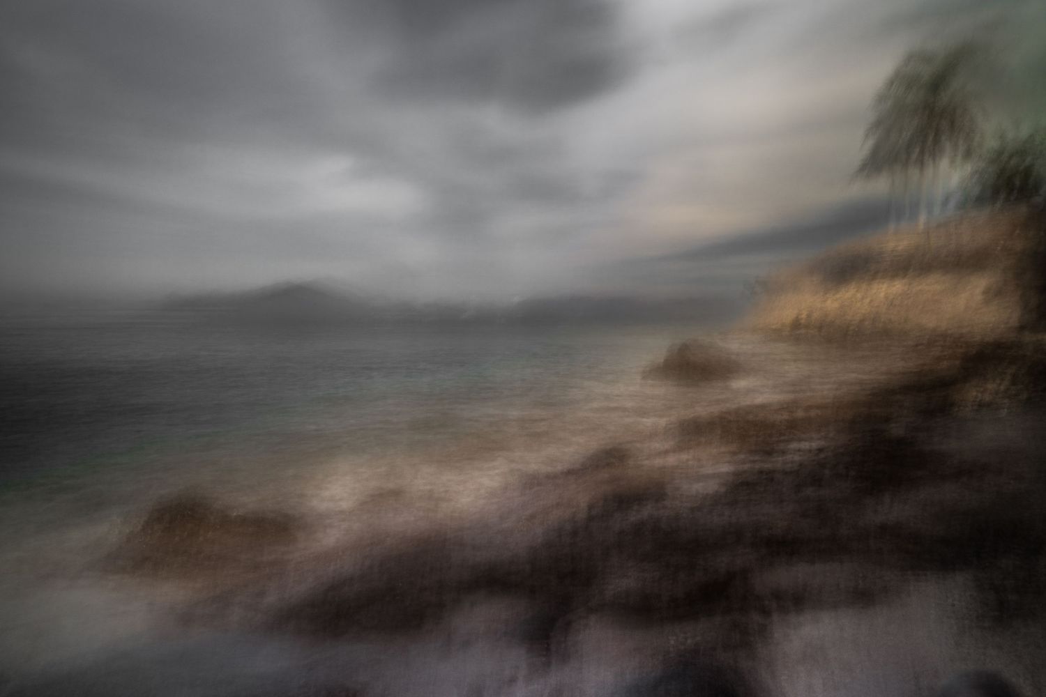 Dramatic seascape with blurred rocky coastline under stormy skies.