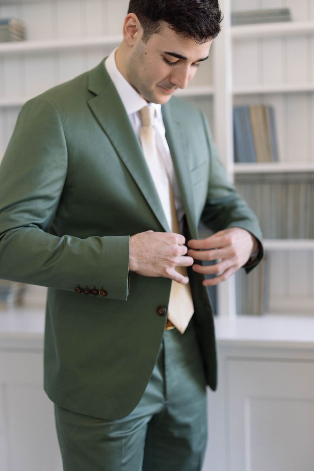 Professional wearing a stylish sage green suit with white shirt and tie adjusts his jacket buttons.