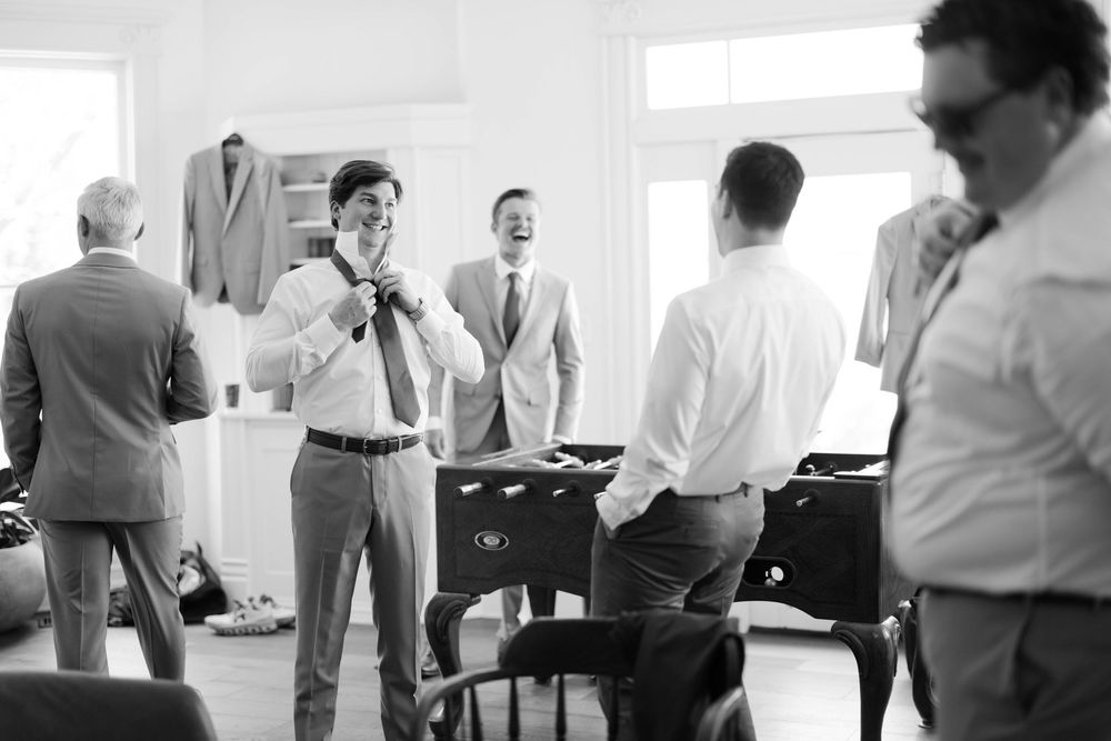 Candid black and white photo showing preparations in a dressing room with multiple people in formal attire adjusting clothing.