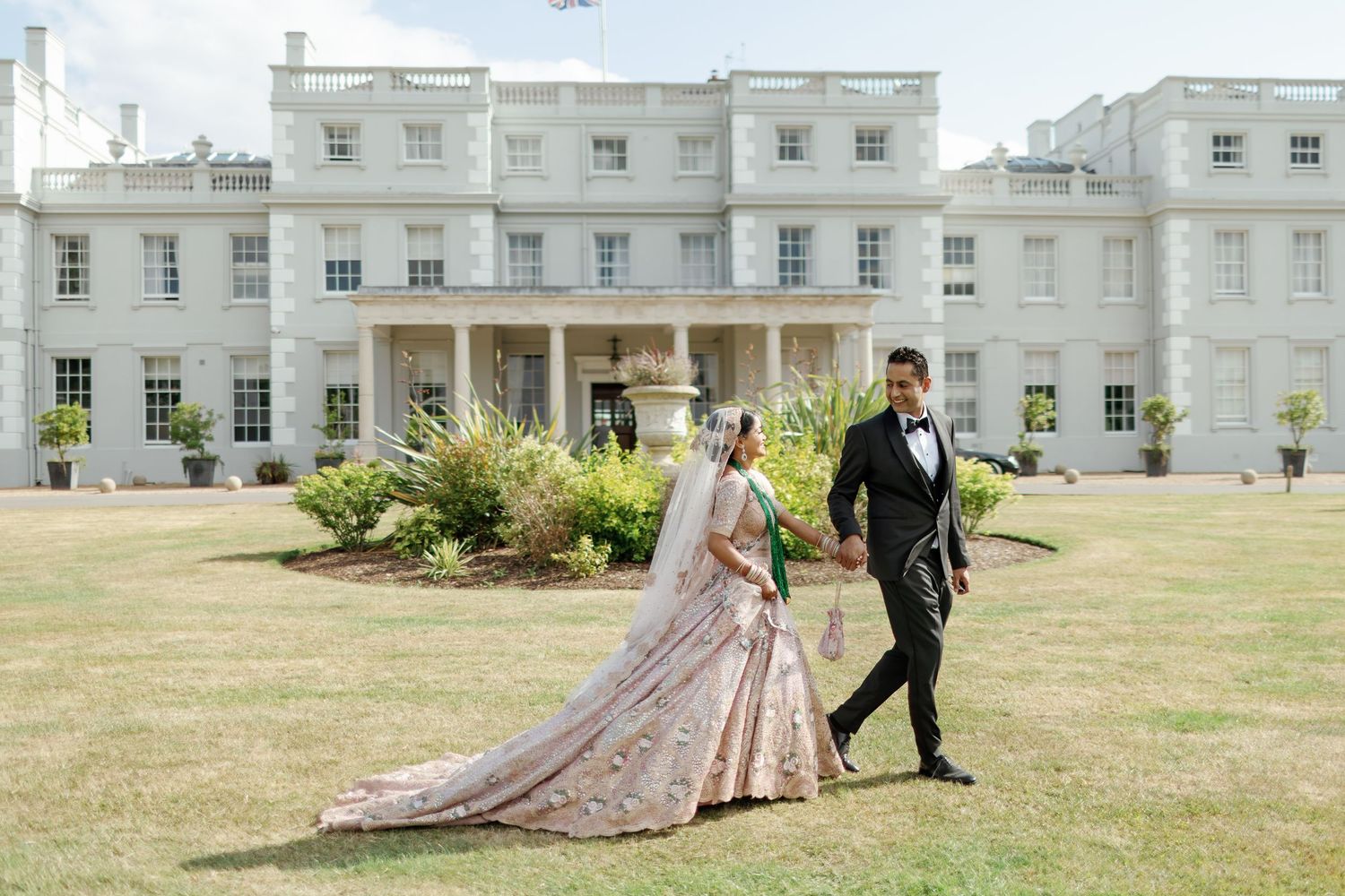 South Asian Bride and groom are walking holding hands at De Vere Wokefield Estate, Berkshire, UK