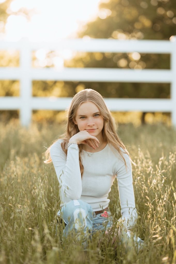 A serene sunset portrait session in a golden meadow with tall grass and a white wooden fence in the background.
