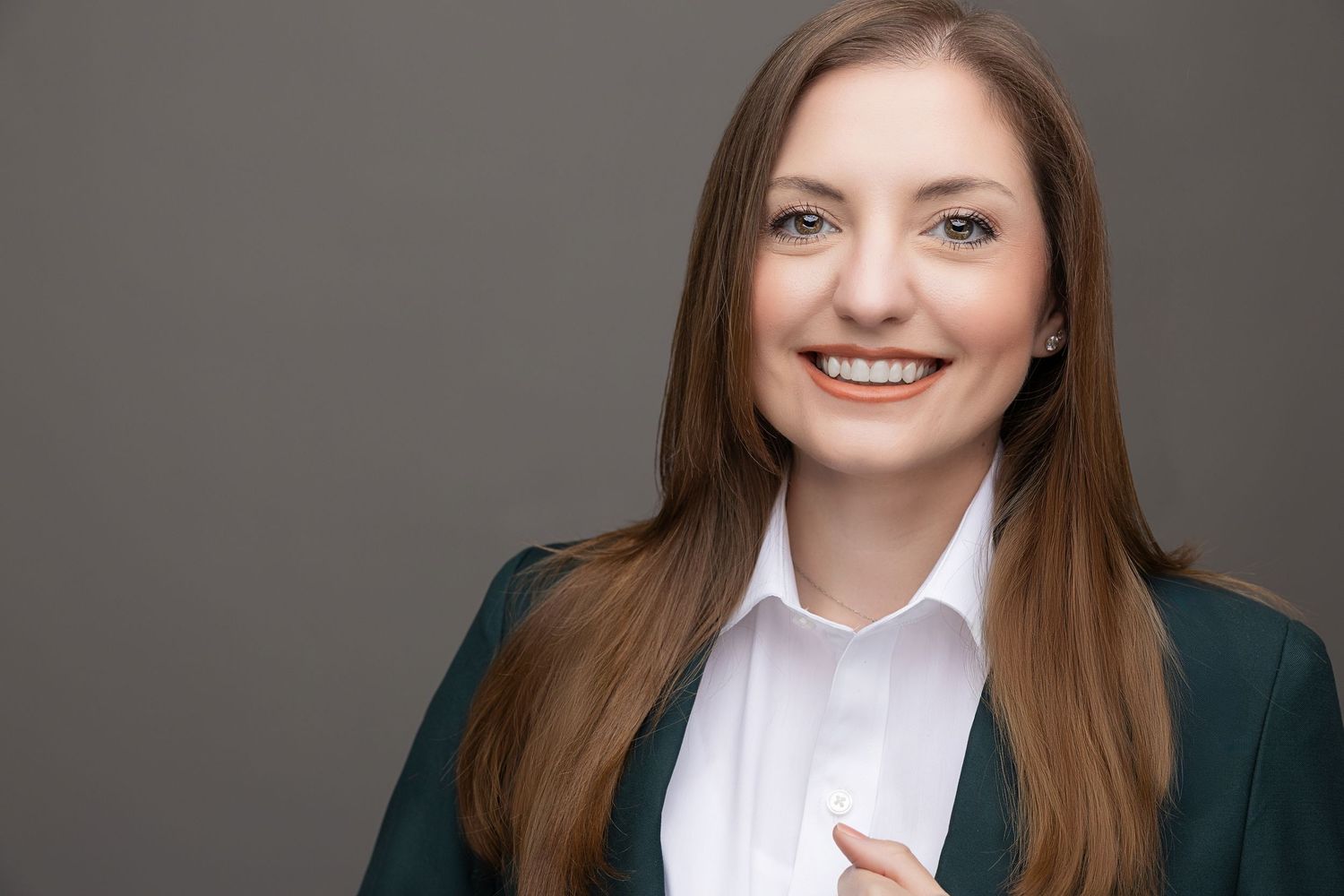 Professional headshot of a person in business attire smiling warmly against a gray background.