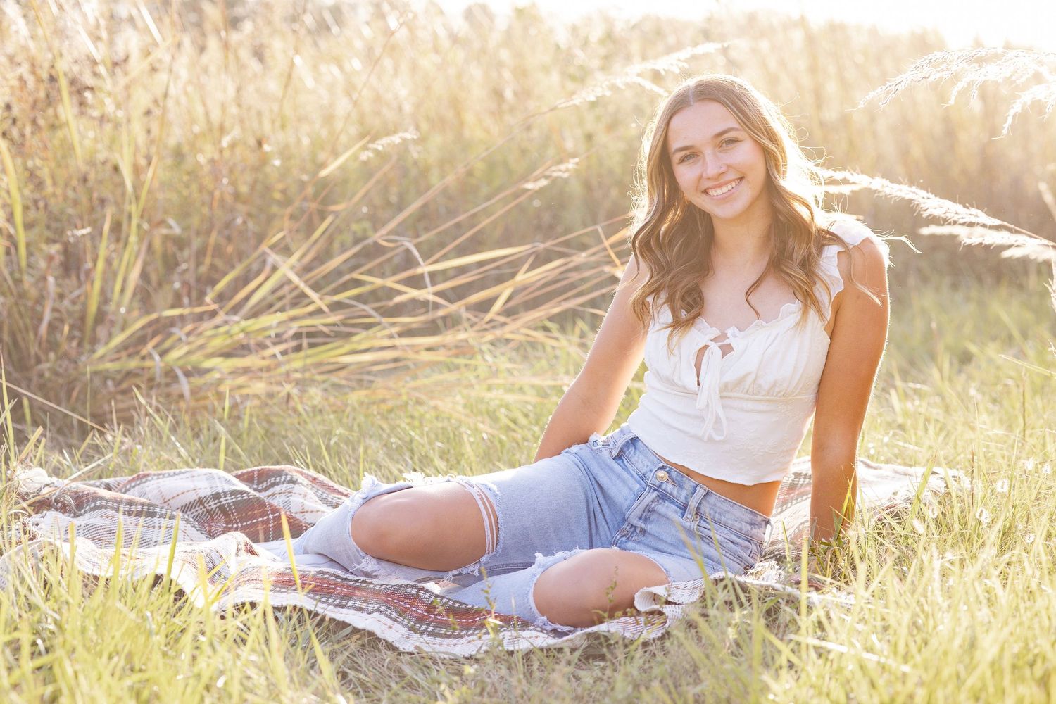 Springfield, IL senior photographer captures a senior sitting in a clearing near tall grass during a session in Central, IL