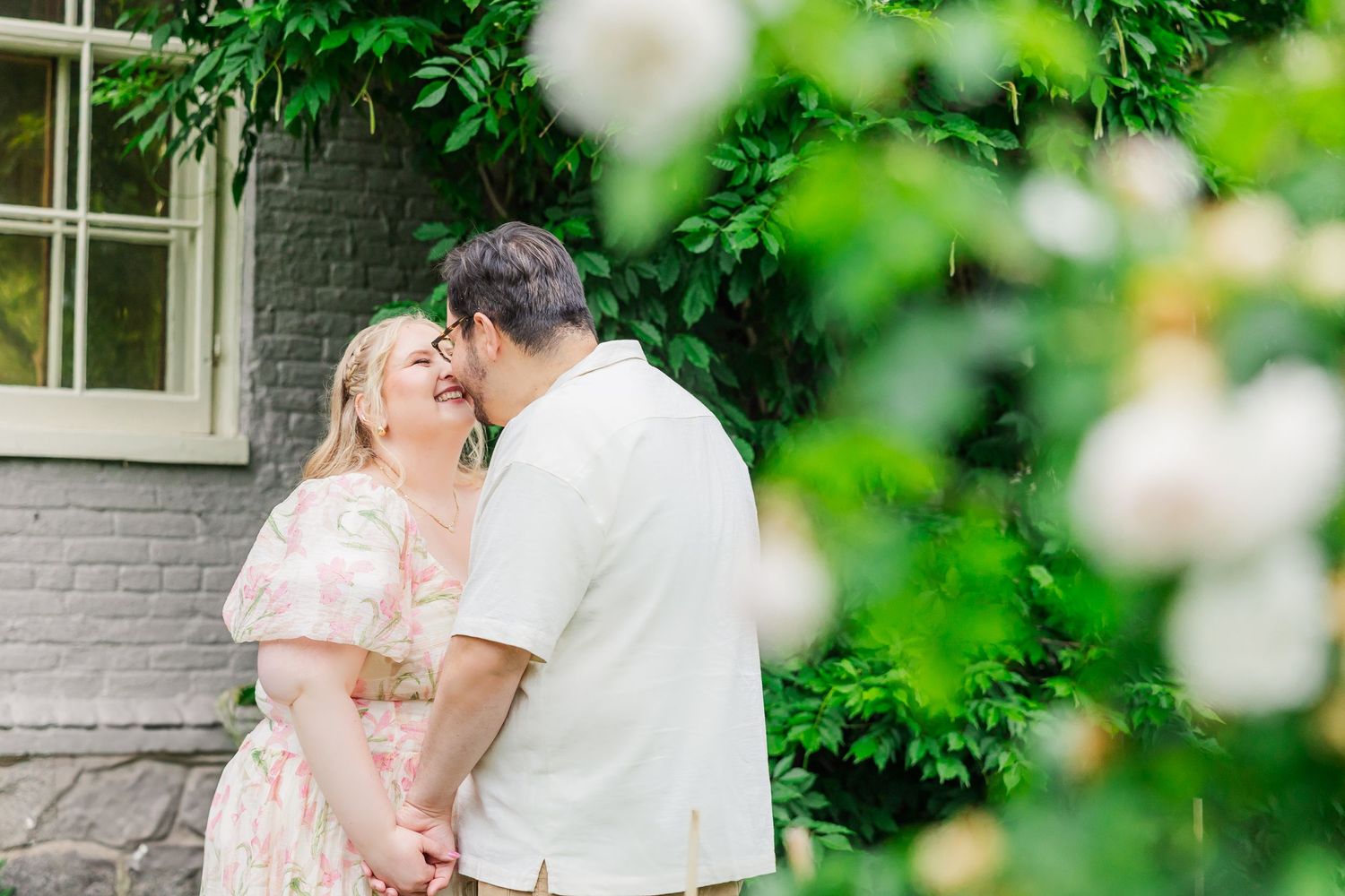 A couple in wedding attire shares a tender moment in a lush garden setting with white blossoms in the foreground.