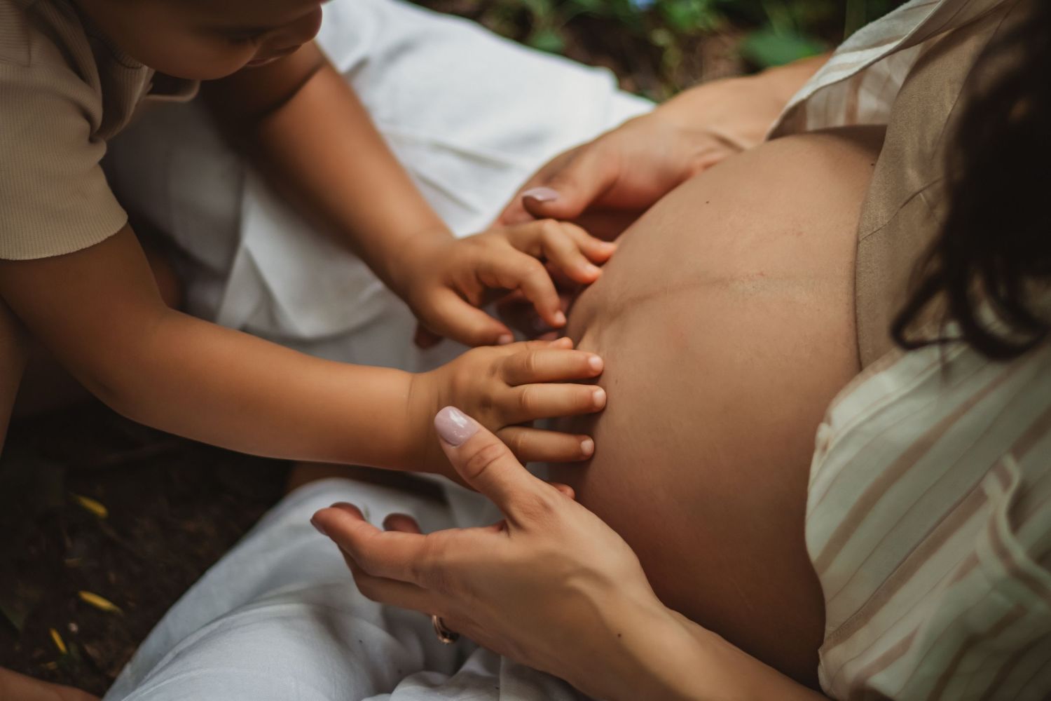 Big bother's gentle hands rest on his mama's pregnant belly during outdoor bare belly maternity photo session.