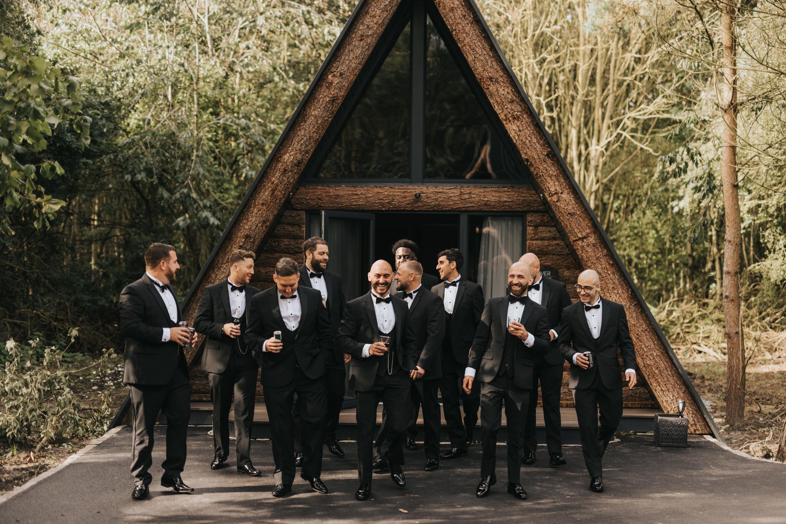 A rustic wood A-frame lodge in the woods serves as a backdrop for a wedding party gathering at Grand Lodge Oaklands.