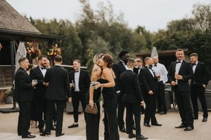 Wedding guests in formal black attire gather outside a rustic venue at Grand Lodge Oaklands - taken by Grimsby photographer.