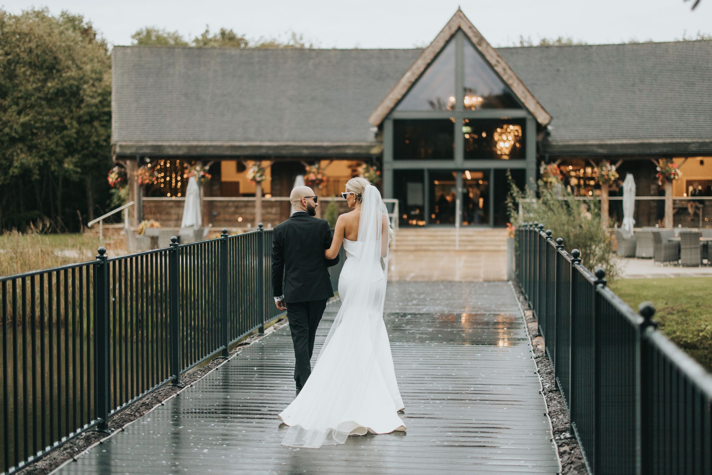 A couple shares a romantic moment on a wet bridge walkway walking towards Grand Lodge Oaklands - taken by Grimsby photographer.