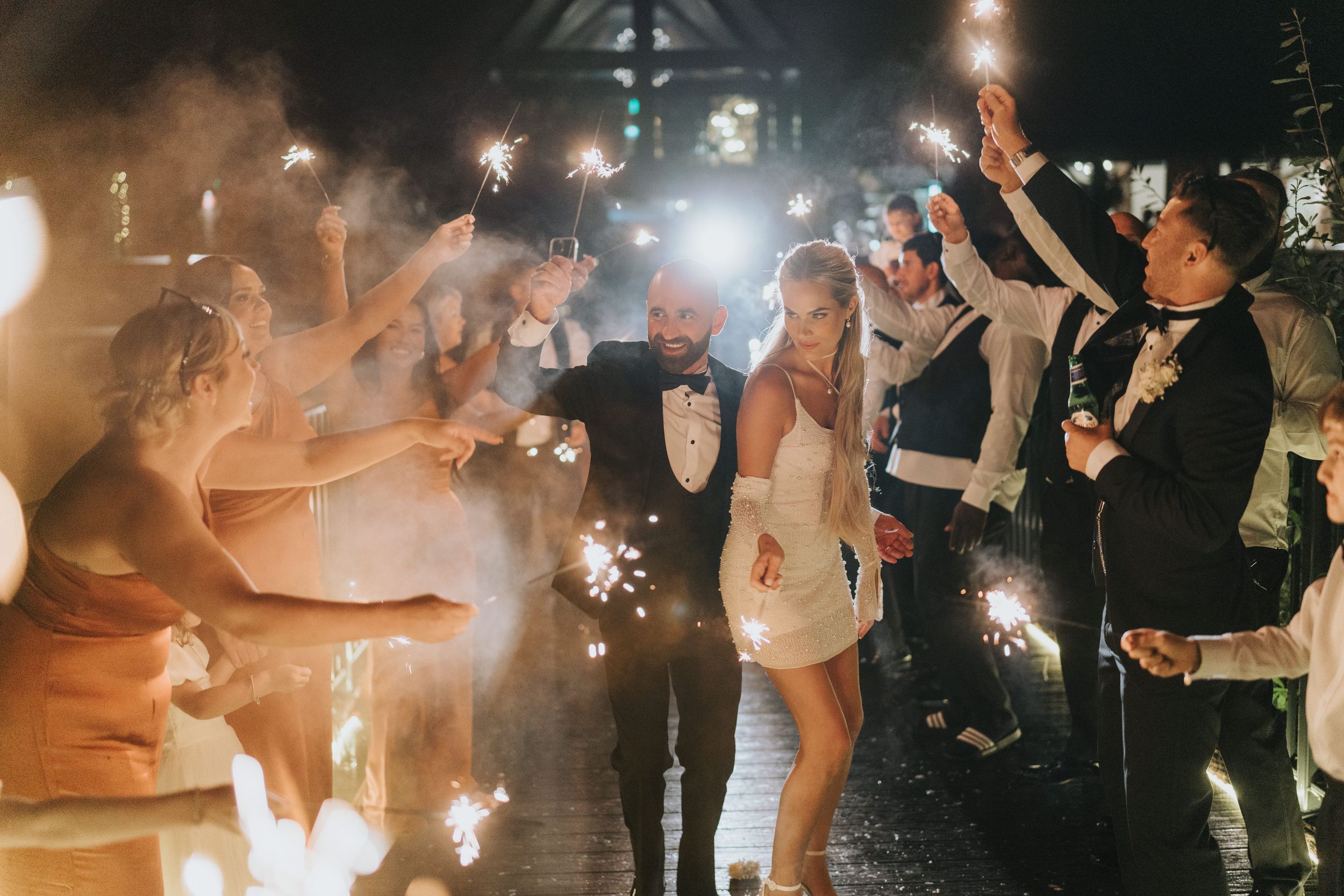 Wedding guests celebrating with sparklers form an illuminated tunnel at an evening reception at Grand Lodge Oaklands.