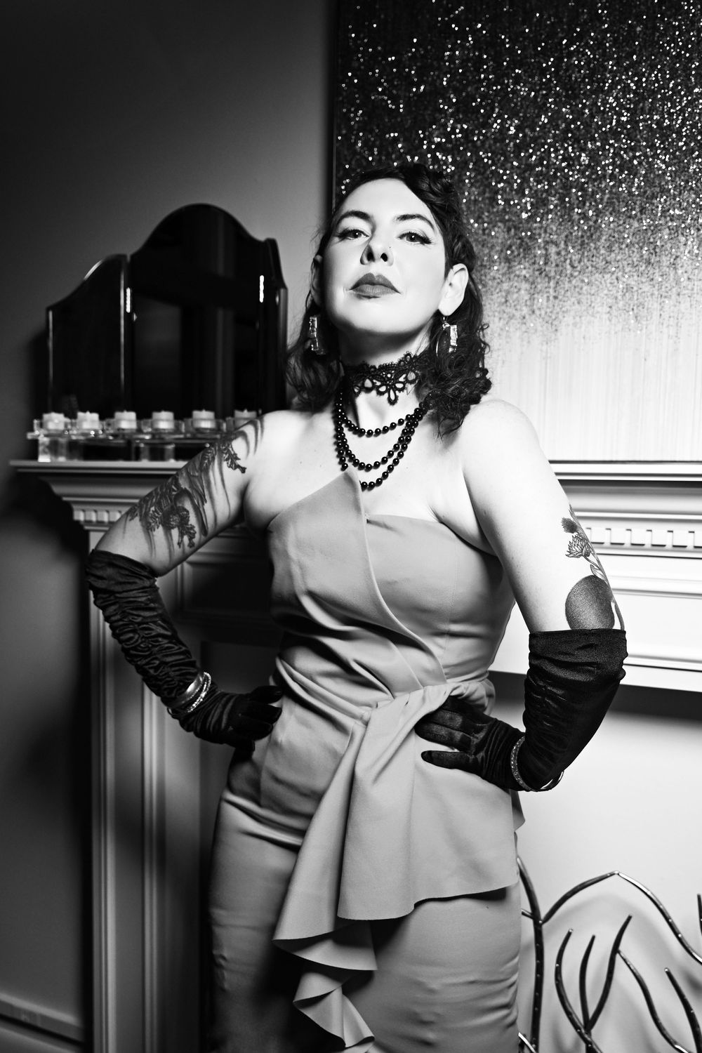 Artistic black and white portrait featuring stylish attire with long gloves, layered necklaces and a fitted dress with ruffle detail.