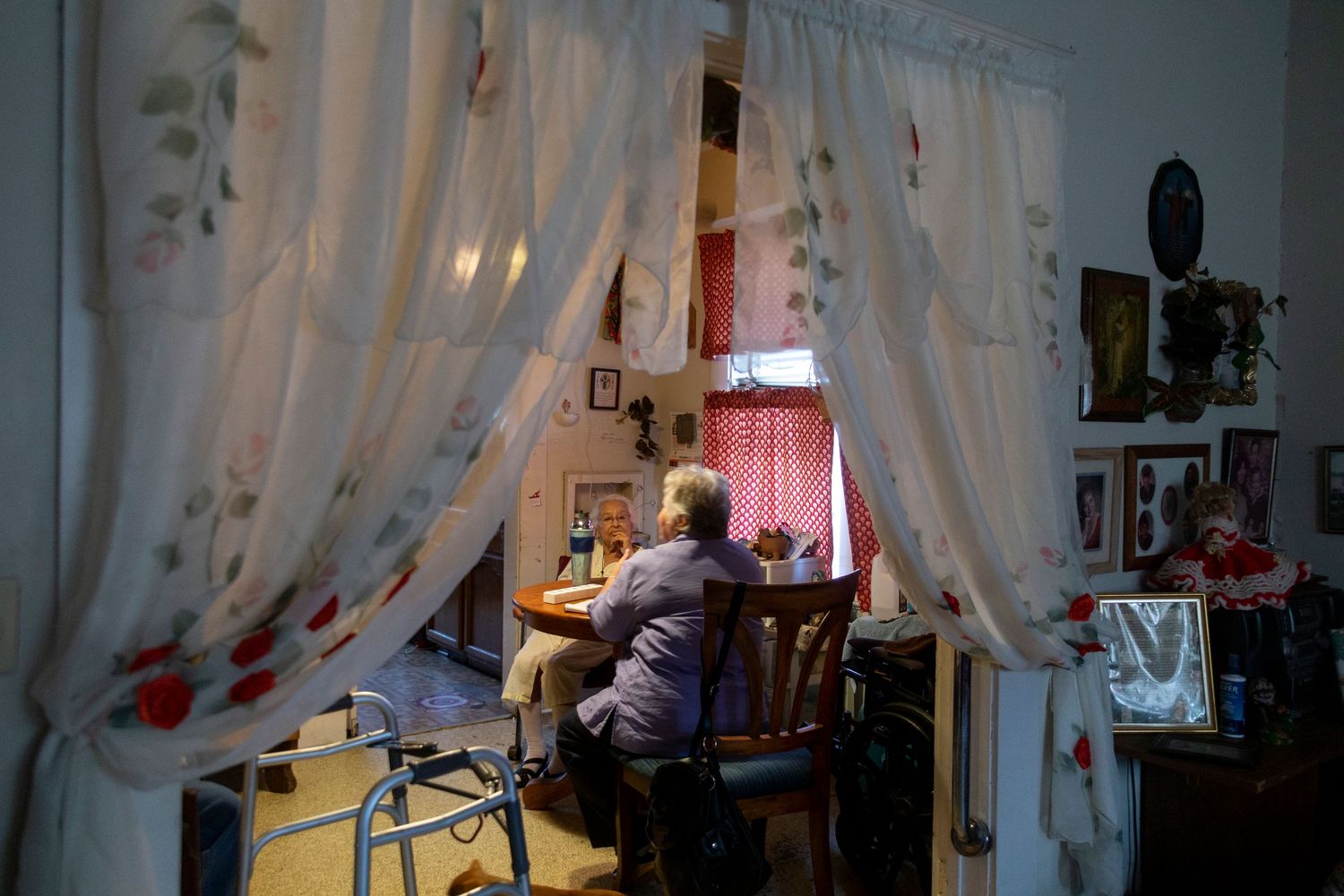 Through sheer floral curtains, a person works at a desk illuminated by soft pink light in a cozy home office space.