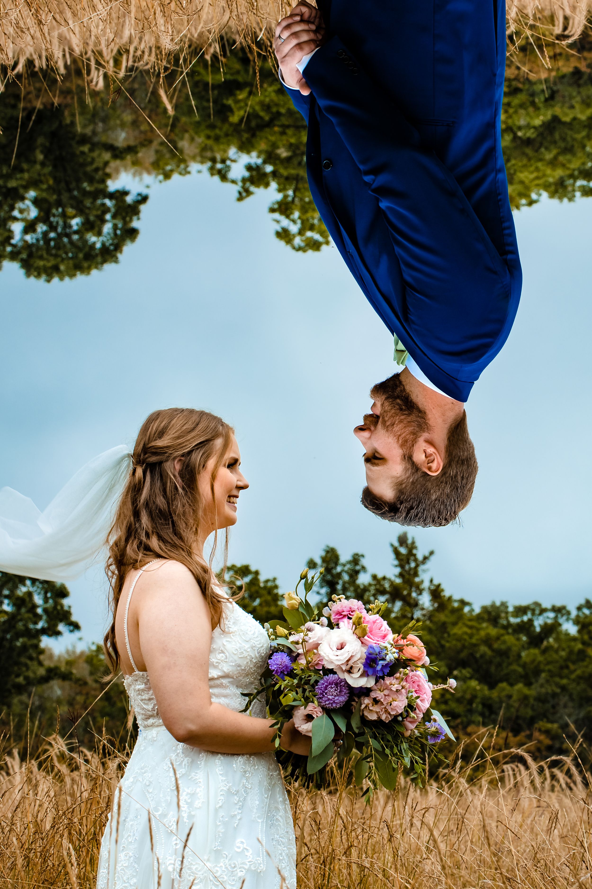 A creative upside-down portrait of a couple with a colorful bouquet in a wheat field.